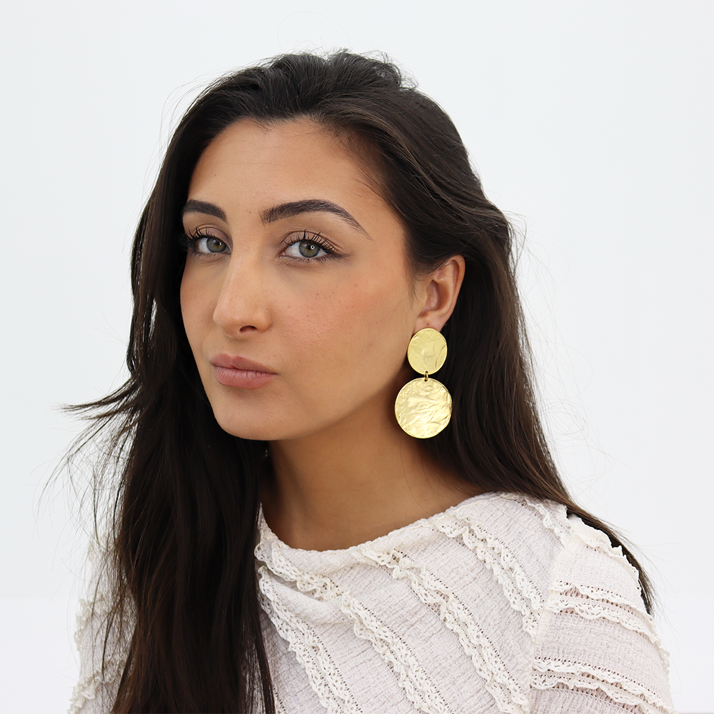 Gold Hammered Disc Statement Earrings worn on brunette model with white textured blouse