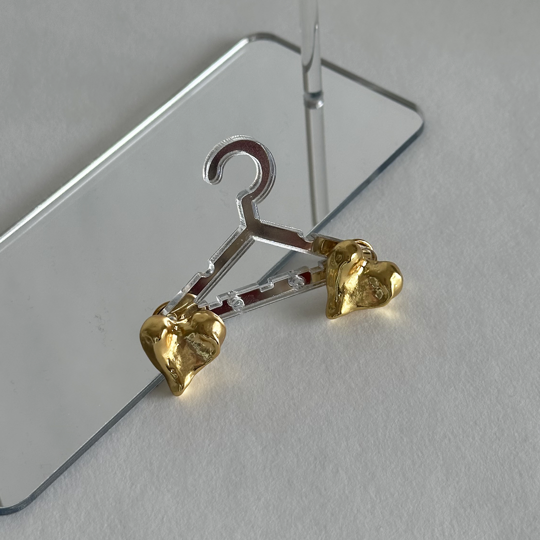 Molten Heart Stud Earrings displayed on a miniature transparent hanger over reflective surface