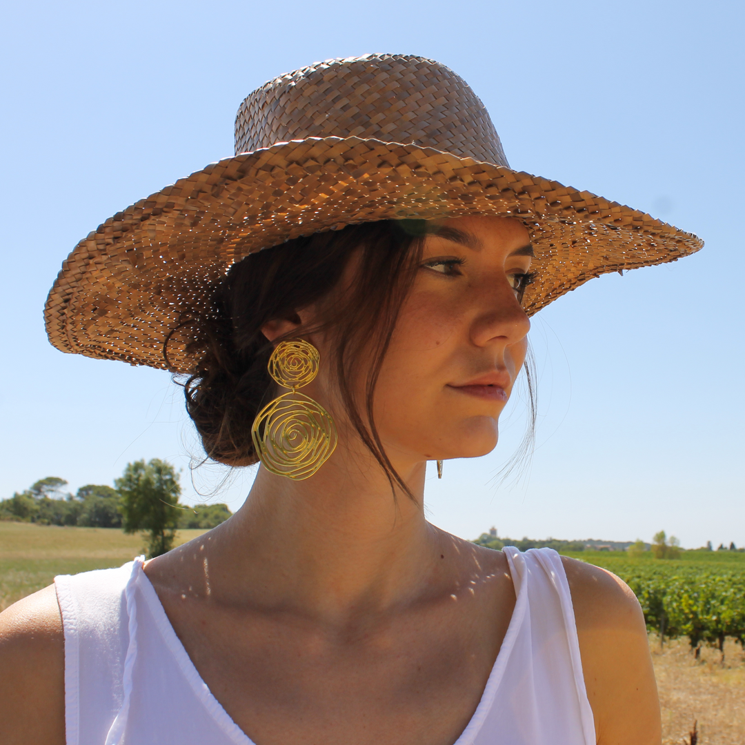 Gold Rose Cut Out Clip-On Earrings worn outdoors with wide straw hat and white top