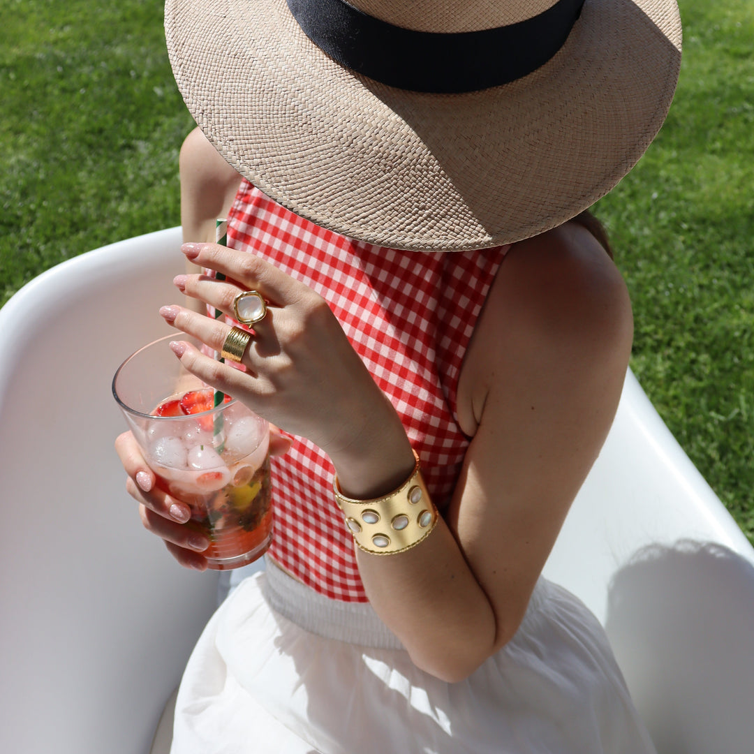 a trendy women wearing statement jewelry by karine sultan, a hat and a red vichy top